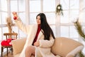 Portrait of elegant young woman wearing white fur coat holding Christmas red ball sitting on sofa in light cold summer Royalty Free Stock Photo