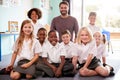 Portrait Of Elementary School Pupils Wearing Uniform Sitting On Floor In Classroom With Male Teacher Royalty Free Stock Photo