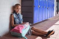 Portrait of elementary schoolgirl using mobile phone while sitting by lockers