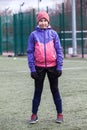 Portrait of eleven-year girl football player standing on grass field in uniform and hobnailed boots