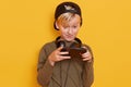 Portrait of emotional and active little boy with blond hair and green shirt, carrying his finger on screen of smartphone while Royalty Free Stock Photo