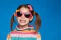 Portrait of an emotional girl of five years old in a striped sweater and in children`s glasses on a blue background Royalty Free Stock Photo