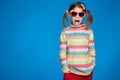 Portrait of an emotional girl of five years old in a striped sweater and in children`s glasses on a blue background Royalty Free Stock Photo