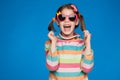 Portrait of an emotional girl of five years old in a striped sweater and in children`s glasses on a blue background Royalty Free Stock Photo