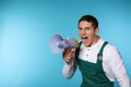 Portrait of emotional male worker using megaphone on color background