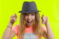 Portrait of an emotional smiling teen girl in hat pointing at the camera, showing hand gesture this is you, over yellow studio Royalty Free Stock Photo