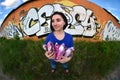 A wide-angle photo of a girl with aerosol paint cans in the hands on a graffiti wall background