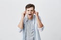 Emotional young male student in blue shirt grimacing, mocking, making faces, pulling ears, sticking out his tongue