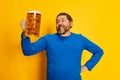 Portrait of emotive, happy man in blue sweater posing with foamy beer glass isolated over yellow background. Favourite Royalty Free Stock Photo