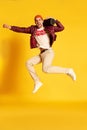 Portrait of emotive happy young man posing in stylish casual clothes, jumping with music player against yellow studio Royalty Free Stock Photo