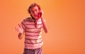 Portrait of emotive young man talking on retro phone, posing isolated over orange studio background in neon light