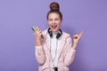 Portrait of energetic lovely young girl with hairdo, getting pleasure, enjoying weekends, holding smartphone, having headphones Royalty Free Stock Photo