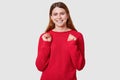 Portrait of energetic woman has brown straight hair, clenches fists with happiness, has toothy smile, dressed casual red sweater, Royalty Free Stock Photo