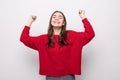 Portrait of energetic woman clenches fists with happiness, has toothy smile, dressed casual red sweater, girl win lottery, Royalty Free Stock Photo