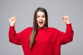 Portrait of energetic woman has brown straight hair, clenches fists with happiness, has toothy smile, dressed casual red sweater, Royalty Free Stock Photo