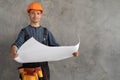 portrait of engineer repairman with house renovation plan in hands on background of concrete wall. The happy builder