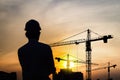 Portrait of engineer silhouette wear a helmet at construction site with crane background and sunset