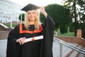 Portrait enthusiastic female college student graduate in cap and gown celebrating, holding diploma.