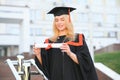 Portrait enthusiastic female college student graduate in cap and gown celebrating, holding diploma.