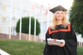 Portrait enthusiastic female college student graduate in cap and gown celebrating, holding diploma.