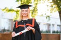 Portrait enthusiastic female college student graduate in cap and gown celebrating, holding diploma.