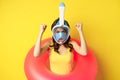 Portrait of enthusiastic young woman on vacation, wearing snorkling, diving mask and swimming ring, standing over yellow