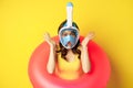 Portrait of enthusiastic young woman on vacation, wearing snorkling, diving mask and swimming ring, standing over yellow