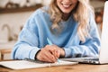 Portrait of european blond woman 20s wearing casual sweatshirt working on laptop and writing down notes at home Royalty Free Stock Photo