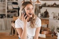 Portrait of european blond woman talking on cell phone while standing in stylish wooden kitchen at home Royalty Free Stock Photo