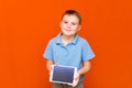 Portrait of european schoolboy with tablet and blue t-shirt on orange studio background