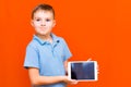 Portrait of european schoolboy with tablet and blue t-shirt on orange studio background