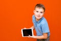 Portrait of european schoolboy with tablet and blue t-shirt on orange studio background