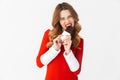 Portrait of european woman 20s wearing Santa Claus red costume smiling and eating chocolate bar, isolated over white background Royalty Free Stock Photo