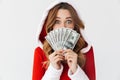 Portrait of european woman 20s wearing Santa Claus red costume smiling and holding fan of money in dollar banknotes, isolated over Royalty Free Stock Photo