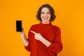 Portrait of european woman holding and demonstrating smartphone while standing isolated over yellow background Royalty Free Stock Photo