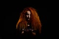 Portrait of an evil red-haired witch conjures in the dark.