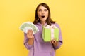 Woman holding wrapped present box and euro banknotes, looking at camera with open mouth. Royalty Free Stock Photo