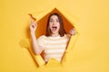 Portrait of excited beautiful woman wearing striped shirt posing in yellow paper hole, having great idea, raising finger up, keeps Royalty Free Stock Photo