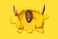 Portrait of excited black man looking through hole in yellow paper, standing with raised arms, screaming happily Royalty Free Stock Photo