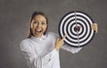 Portrait of excited businesswoman pointing finger at target with dart right in bullseye