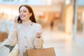 Portrait of excited cheerful young woman holding shopping paper bags and talking using mobile phone, discussing Royalty Free Stock Photo