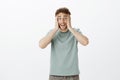 Portrait of excited crazy european guy in t-shirt, holding hands on face and smiling with weird funny expression, being