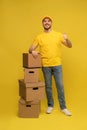 Portrait of excited delivery man in yellow uniform holding paper box isolated over yellow background.