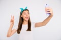 Portrait of excited enthusiastic girl feel positive cheerful emotions take selfie on her smartphone make v-sign greet