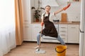 Portrait of excited extremely happy housewife wearing white t shirt, jeans and brown apron, washing floor with mop and dancing, Royalty Free Stock Photo