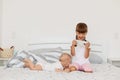 Portrait of excited female child wearing white t shirt and pink shorts playing video games on cellphone, cute infant baby lying on Royalty Free Stock Photo