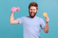 Man in T-shirt holding tasty cooky and raised hand with pink dumbbell, screaming, burning calories.