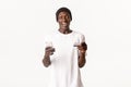 Portrait of excited, happy african-american young male student, holding credit card and smartphone with amused smile Royalty Free Stock Photo