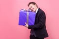 Portrait of excited happy young man in suit hugging big gift and smiling. studio shot isolated on pink background Royalty Free Stock Photo