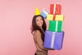 Portrait of excited joyful young woman wearing party cone and smiling pleased as holding mount of gift boxes Royalty Free Stock Photo